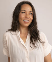 A woman with long hair smiles, wearing a blouse, embodying the spirit of WeNatal's holistic approach to prenatal wellness and lifestyle.